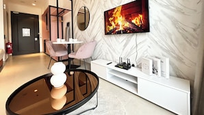 Una sala de estar moderna con un televisor de pantalla plana mostrando una chimenea, una mesa de centro redonda de vidrio y un mueble de entretenimiento blanco.