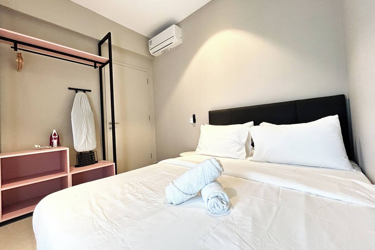 A hotel room with a neatly made bed, a built-in shelf with a mirror, and an air conditioning unit on the wall.