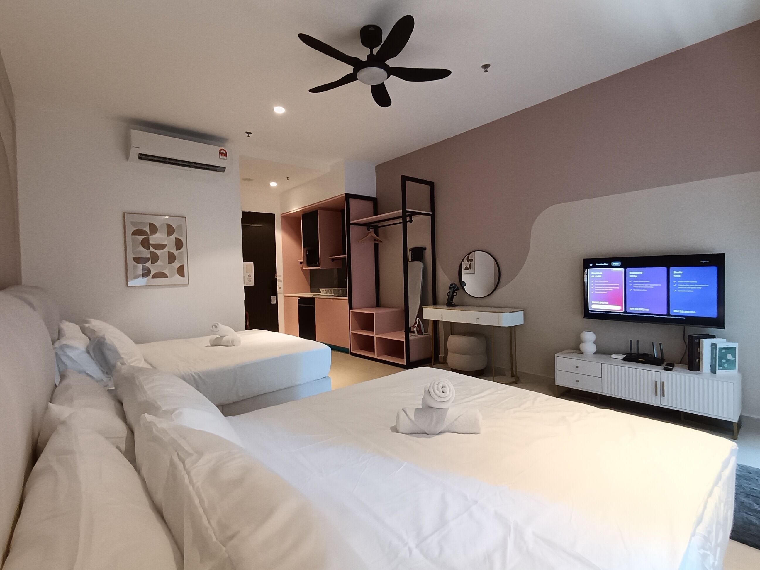 A modern hotel room with two beds, a ceiling fan, a TV, a small desk, and a walk-in closet.