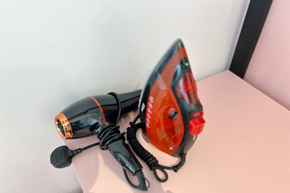 A black and orange hairdryer with a red light on a white surface.