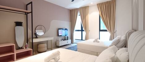 Une chambre d’hôtel avec deux lits, un bureau avec une télévision, un ventilateur de plafond et de grandes fenêtres avec des rideaux.