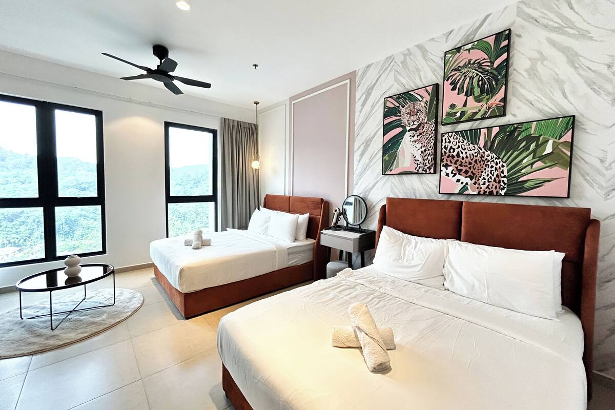 A hotel room with two beds, a ceiling fan, large windows, and tropical-themed artwork on the wall.