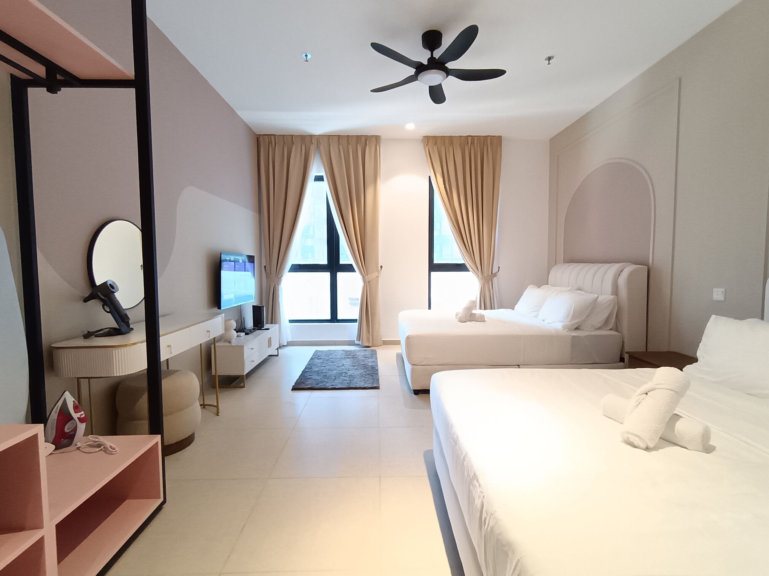 A modern hotel room with a large bed, a desk with a flat-screen TV, a ceiling fan, and large windows with curtains.