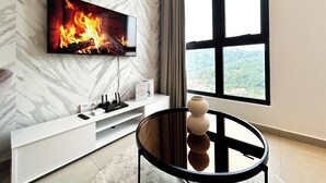 Un salón moderno con un televisor grande mostrando una chimenea, un mueble blanco para entretenimiento y vistas a un paisaje verde a través de un ventanal.