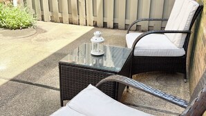 Un patio con mobiliario de mimbre, una mesa de vidrio y un farol.