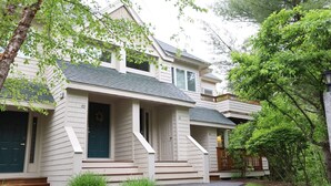 A two-story house with a front porch, a visible front door, and a small front yard with grass and shrubs. - Forest Knoll M4, Waterville Valley (Waterville Valley)