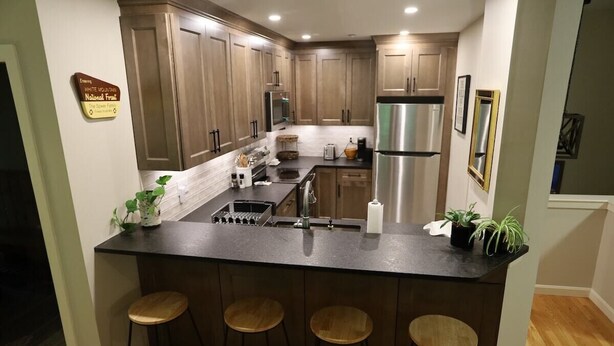 A kitchen with wooden cabinets, a stainless steel refrigerator, a coffee maker, and a sign on the wall. - Forest Knoll M4, Waterville Valley (Waterville Valley)