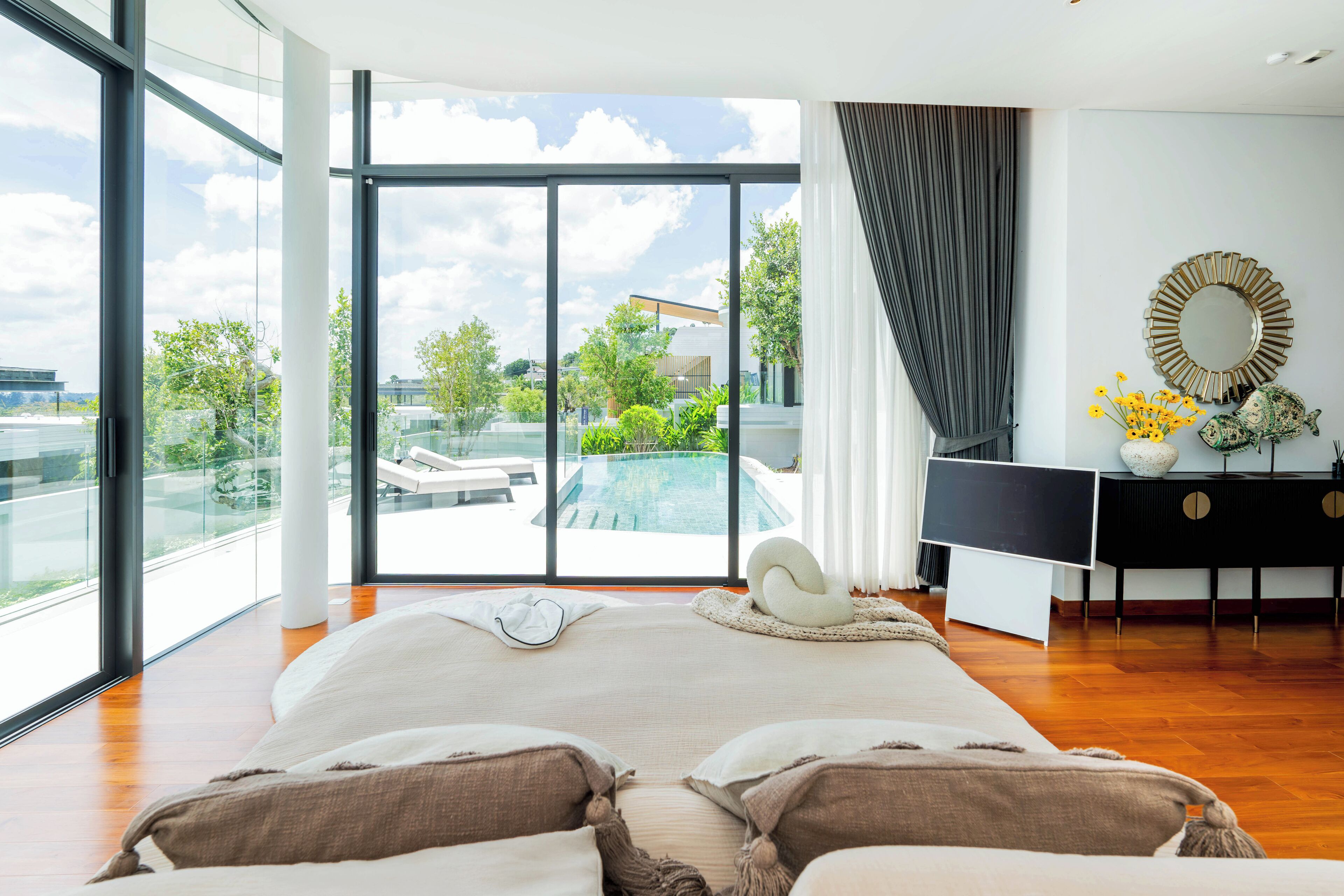 A spacious bedroom with a large bed, a view of a swimming pool, and a modern bathroom with a mirror and decorative items.