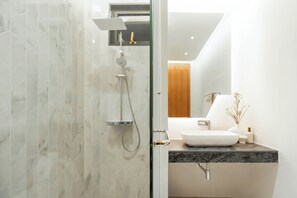 A modern bathroom with a glass door, a white sink, and a shower with a handheld showerhead. - Zavaya Villa (Choeng Thale)