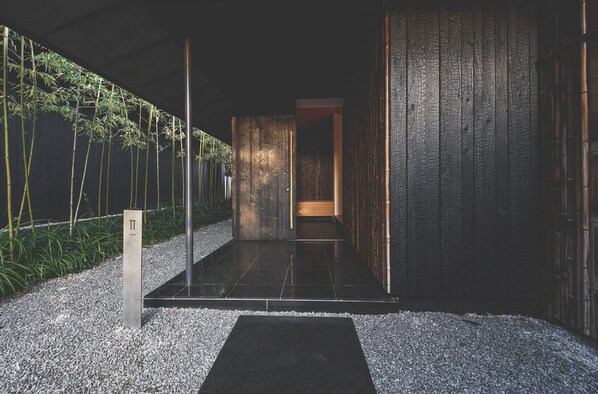 A modern interior with a dark wooden wall, a bamboo plant, and a tiled floor. - COMICO ART HOUSE YUFUIN (Yufu)