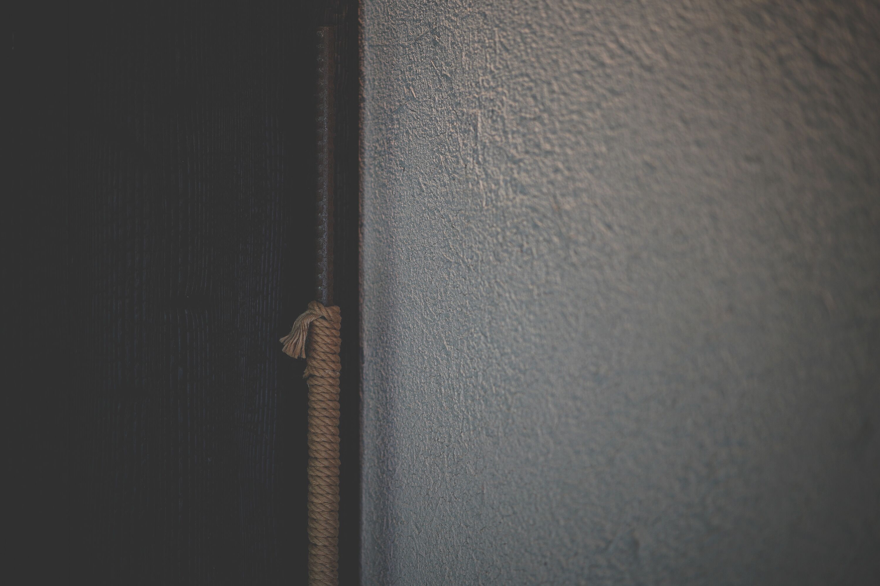 Detalle de una pared texturizada con una cuerda atada a una superficie oscura.