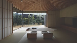A minimalist room with tatami flooring, a low table, and a sliding glass door leading to a garden.