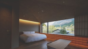 A bedroom with a large window, a bed, and a wooden table.