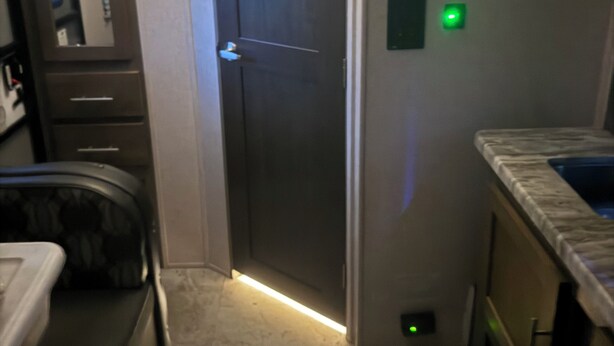 A narrow hallway with a closed door, a small green light, and a microwave on the wall. - Delightful mobile home with AC in Muskegon (Muskegon)