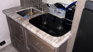 A compact kitchen with a sink, a dishwasher, and a countertop with a dish rack. - Delightful mobile home with AC in Muskegon (Muskegon)