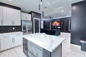 Una cocina moderna con gabinetes blancos, una isla grande, electrodomésticos de acero inoxidable y una pared de acento negra.