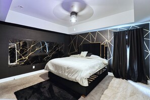Een moderne slaapkamer met een bed, een plafondventilator, een aan de muur hangend kunstwerk en een wand met een geometrisch patroon.