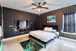 Un dormitorio con cama, ventilador de techo, obras de arte en las paredes y una ventana con cortinas.