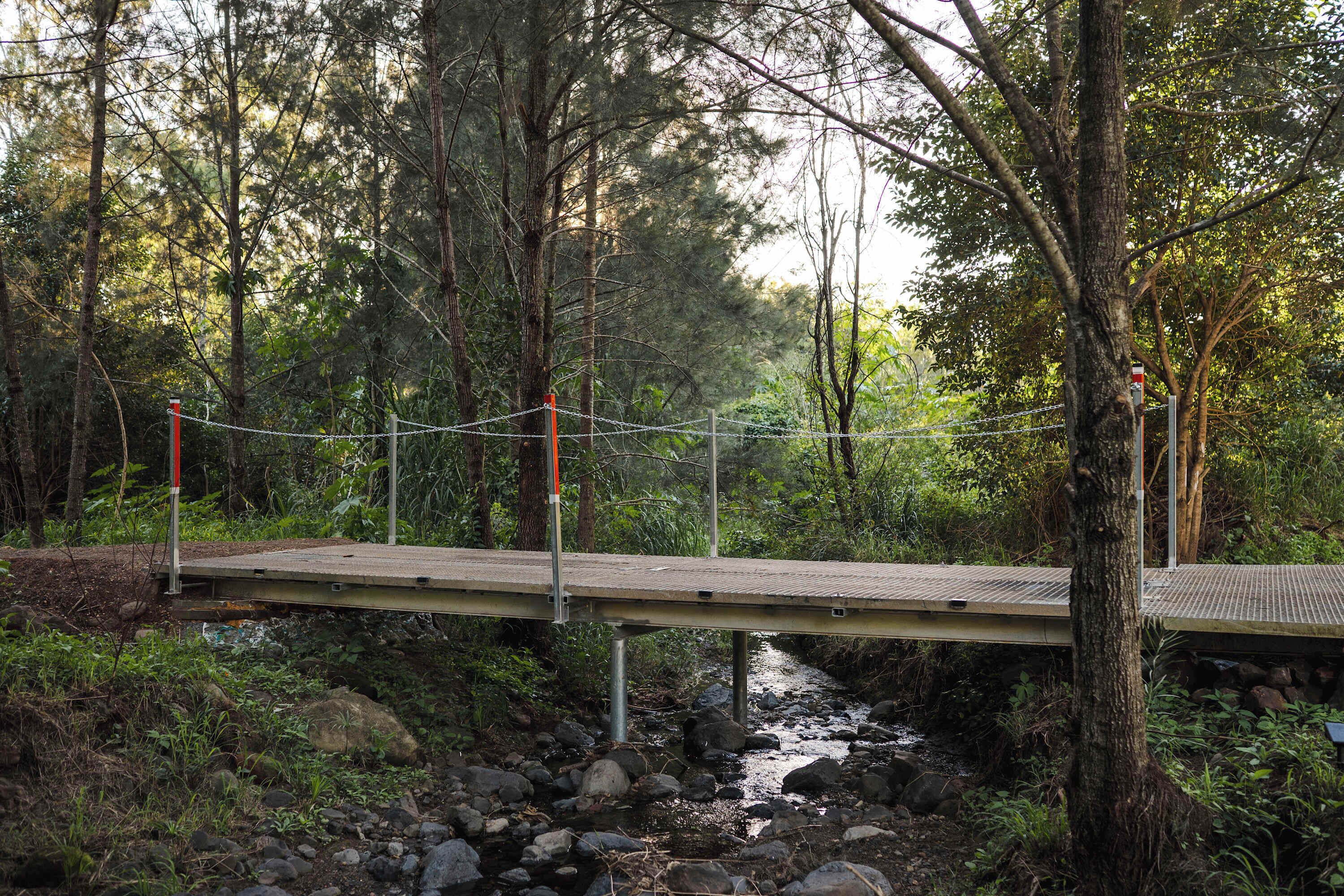 Een houten brug over een beek met rotsen in een bebost gebied.