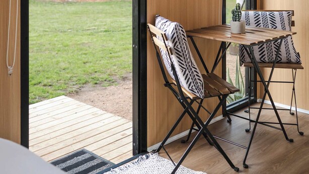 A room with a large sliding glass door leading to a garden, a small table with chairs, and a ceiling-mounted device.