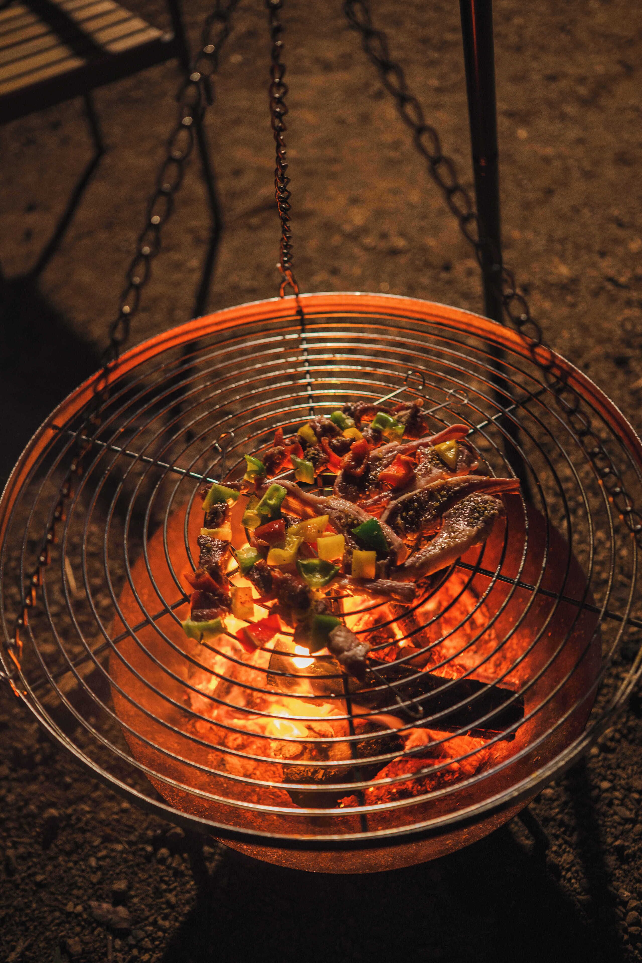 Un barbecue avec divers légumes et morceaux de viande en train de cuire sur une flamme nue.