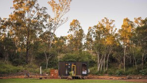 A small cabin with a yellow door, surrounded by trees and a grassy area.