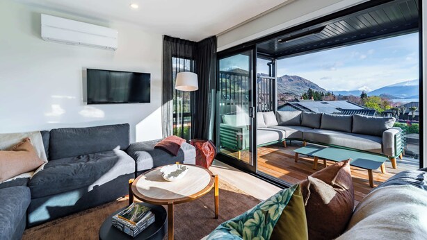 A modern living room with a sofa, coffee table, and a view of mountains through large windows. - Tiro Nui in the Heart of Wanaka (Wānaka)