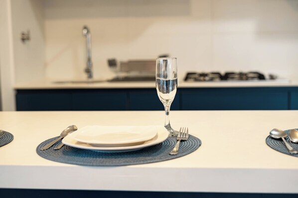 A neatly set dining table with a glass of water, plates, cutlery, and a blue placemat.
