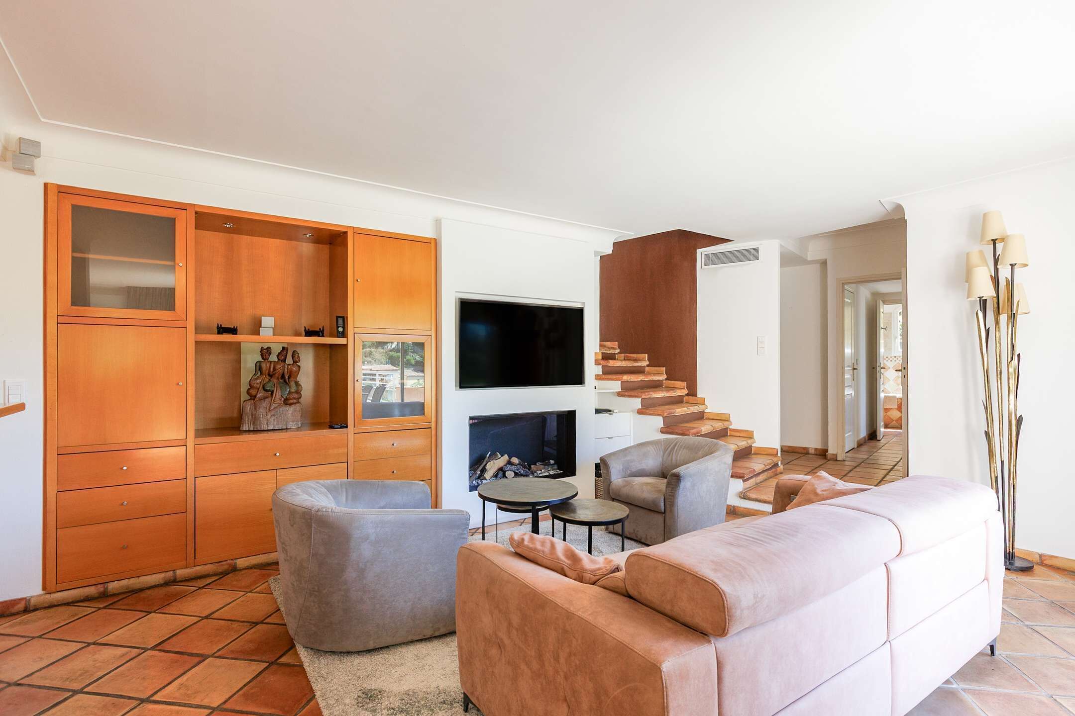 Un salon moderne avec un canapé, des fauteuils, un téléviseur, une cheminée et un meuble en bois.