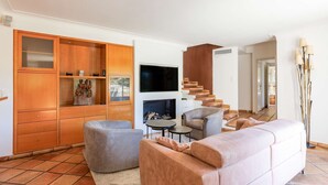 A modern living room with a sofa, armchairs, a TV, a fireplace, and a wooden cabinet.