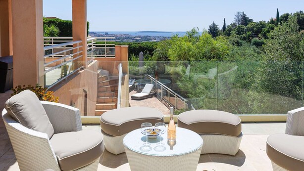 A balcony with wicker furniture, a glass table, and a candle.