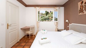 A hotel room with a bed, a desk, a chair, and a window with a view of greenery.