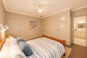 A bedroom with a bed, a ceiling fan, a nightstand, a lamp, a framed picture, and a wardrobe.