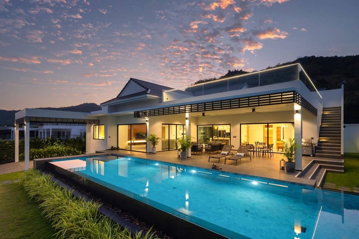 Una casa moderna con piscina, mobiliario exterior y un patio cubierto.
