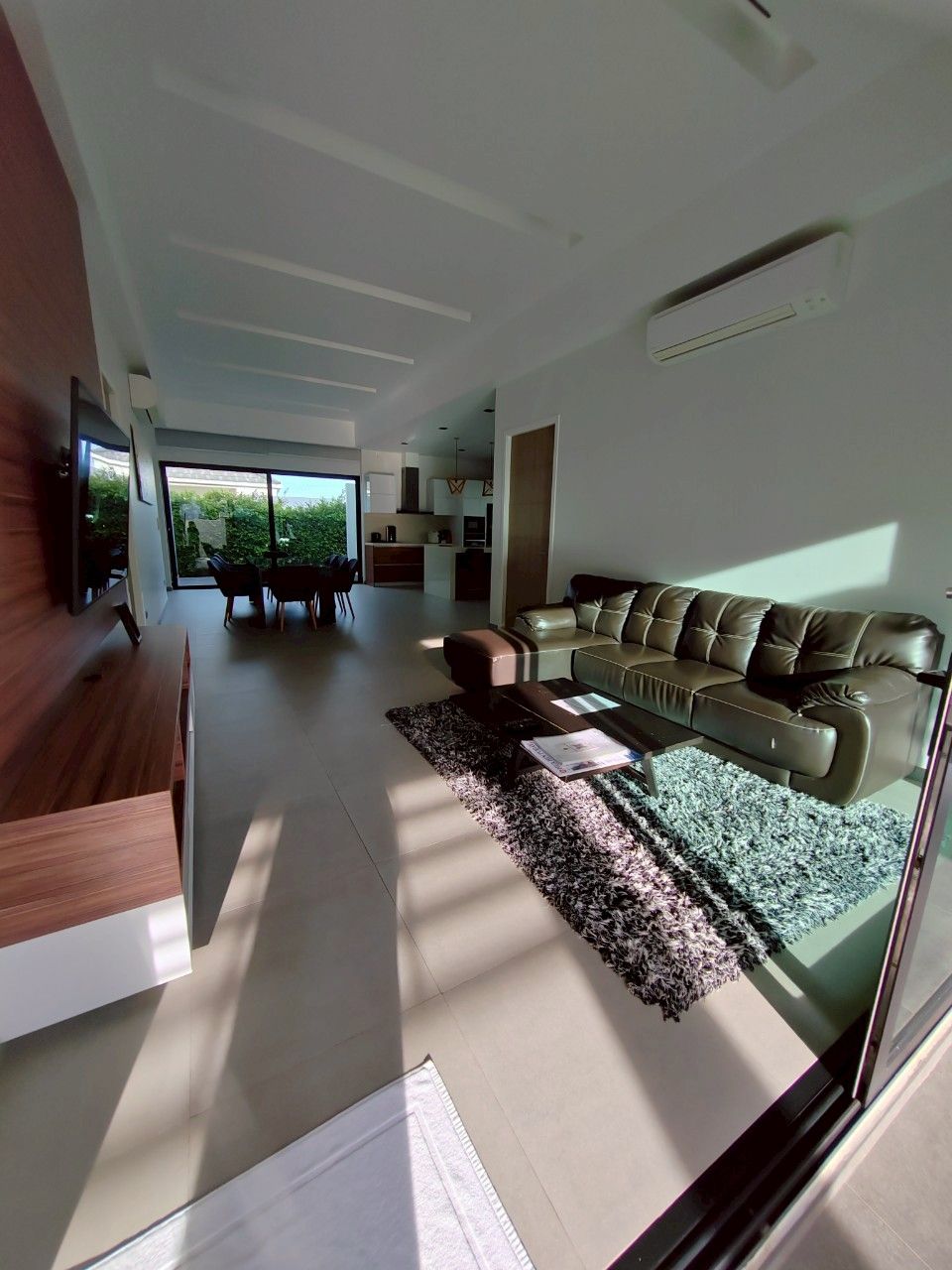 A modern living room with a leather sofa, a flat-screen TV mounted on the wall, and a dining area with a table and chairs.