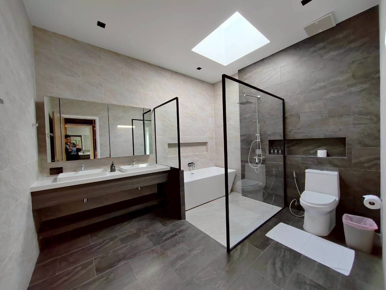 A modern bathroom with a large mirror, a bathtub, a shower enclosure, and a toilet.