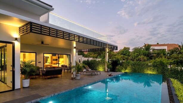 Una casa moderna con piscina, mobiliario exterior y un patio cubierto.