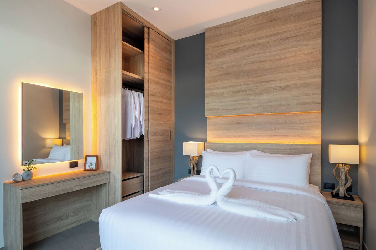 Una habitación de hotel con cama, mesita de noche, armario y una lámpara de pared.