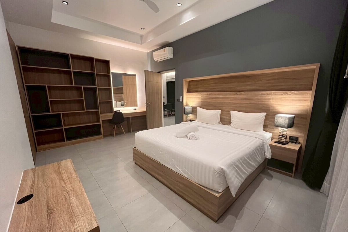 Un dormitorio moderno con una cama grande, cabecero de madera, mesitas de noche con lámparas, un escritorio y un armario empotrado.