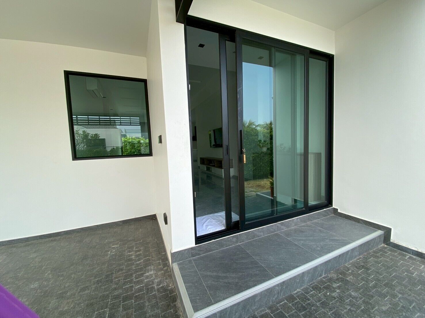 A modern building with a large sliding glass door leading to a covered outdoor area.