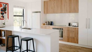 A modern kitchen with a central island, wooden cabinets, and a large window. - Nelson Central Town House (Nelson)