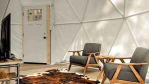 A tent with a white door, two grey chairs with wooden frames, a cowhide rug, and a television on a wooden table. - Cozy Chalet & Luxe Domes Retreat w/Stunning Views (Augusta)