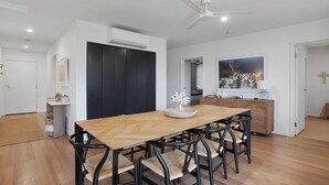 Un área de comedor moderna con una mesa de madera y sillas negras, un equipo de aire acondicionado y un ventilador de techo.