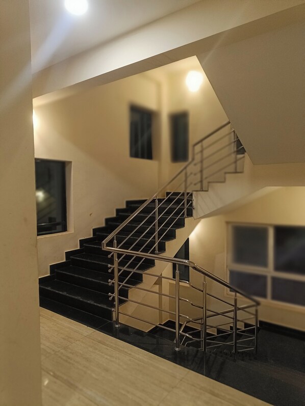 A modern interior with a staircase featuring metal railings and black steps, leading to an upper floor. - Hotel Radhma Residency (Udupi)