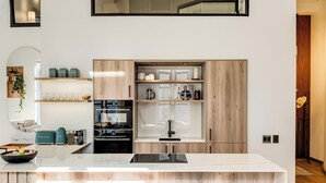A modern kitchen with a central island, wooden cabinetry, and a built-in oven. - Contemporary 2bed in Art Deco Heritage Site Elevea (Cape Town)