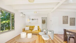 A modern living room with a yellow sofa, grey armchairs, a round coffee table, and a dining table with chairs.