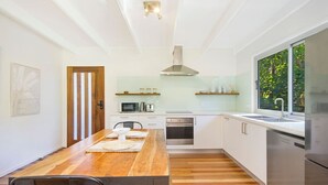 A modern kitchen with white cabinets, a wooden dining table, and a large window.