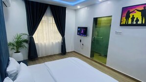 Habitació d'hotel moderna amb un llit gran, un televisor de pantalla plana, un quadre i una porta verda.