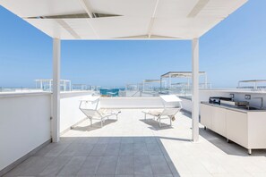 A rooftop terrace with a clear view of the sea, a bar area, and two lounge chairs.