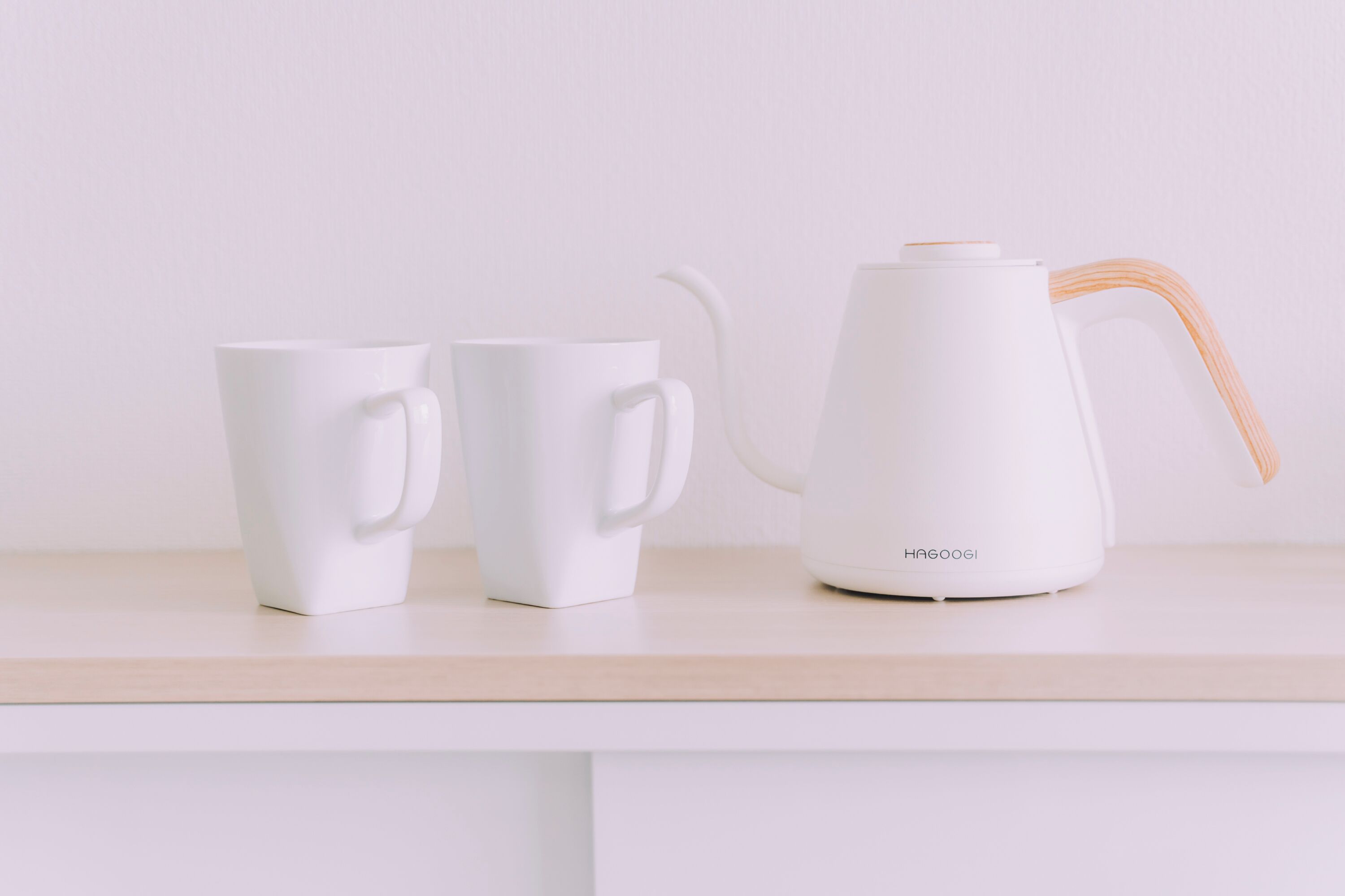 Una tetera eléctrica blanca y dos tazas blancas sobre una encimera de color claro.
